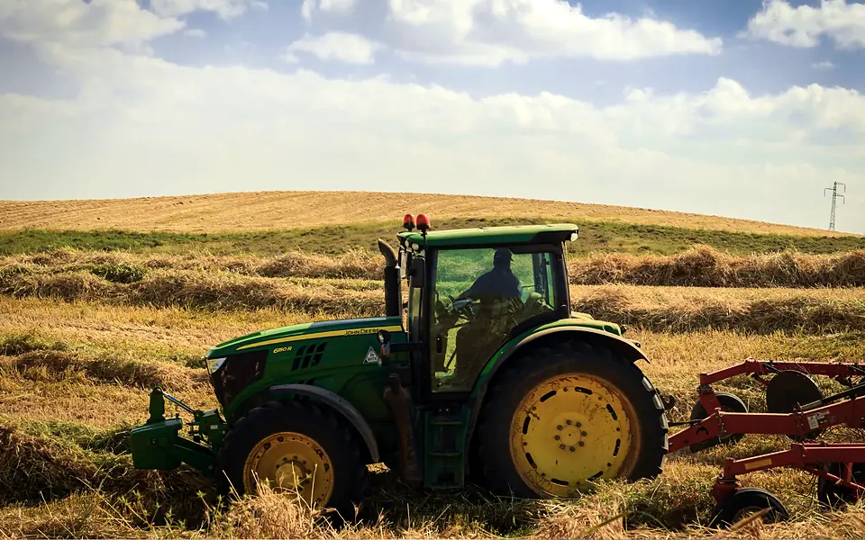 Farmer driving a green tractor that pulls a hay rake across a field