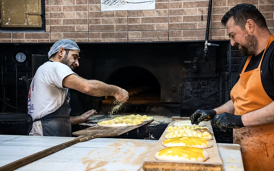 Bakers preparing flatbreads beside a brick oven