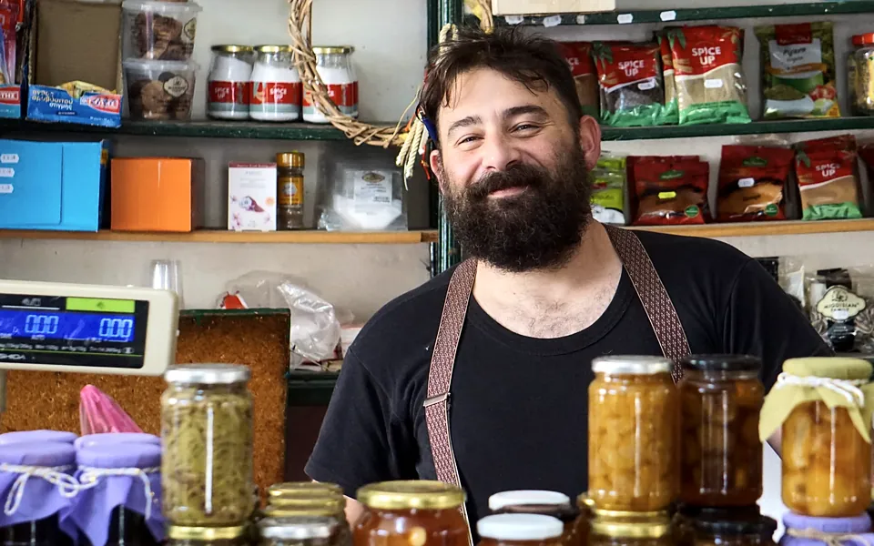 Shop owner smiling behind a counter stacked with jars of preserves