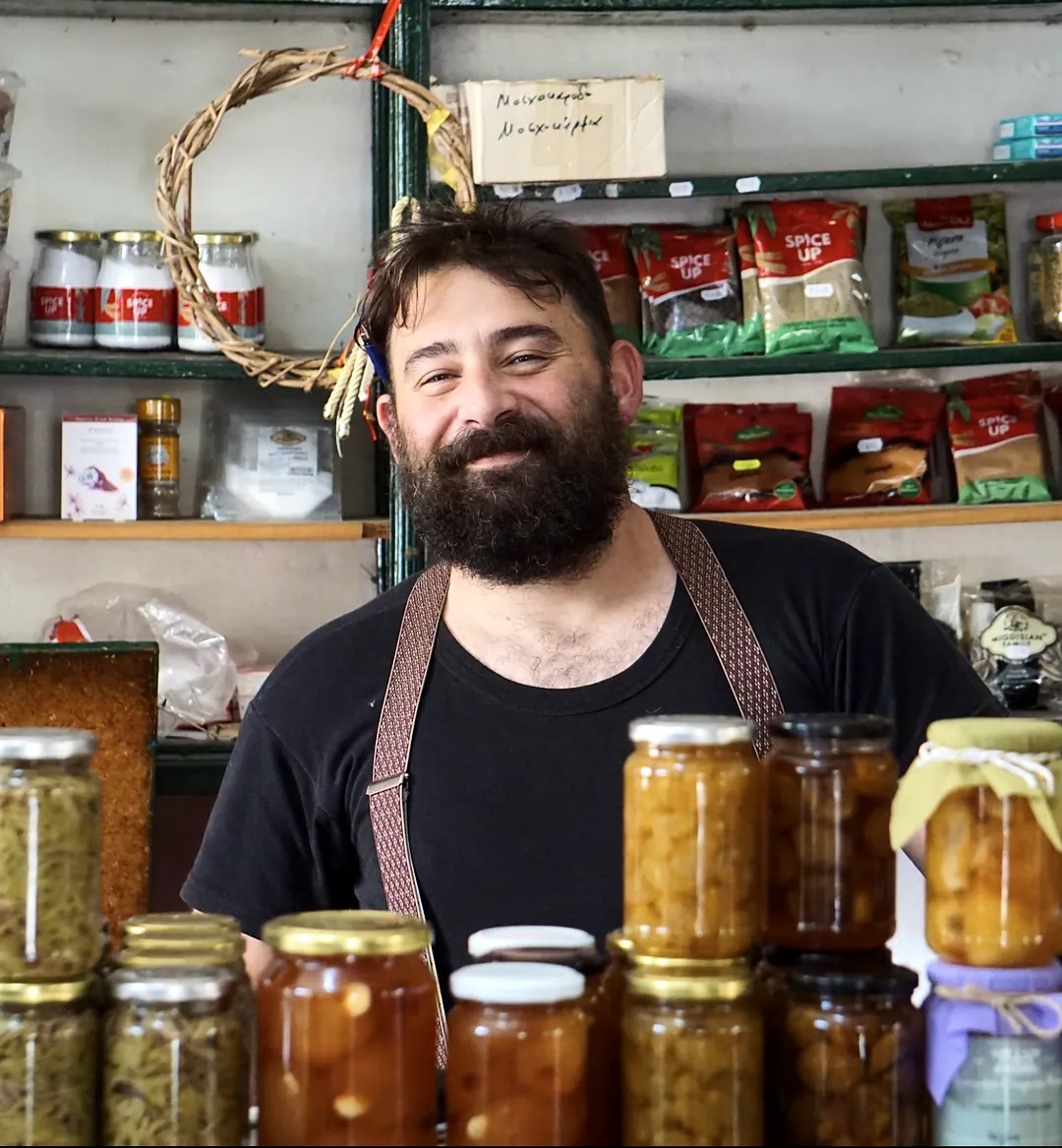 Shop owner smiling behind a counter stacked with jars of preserves