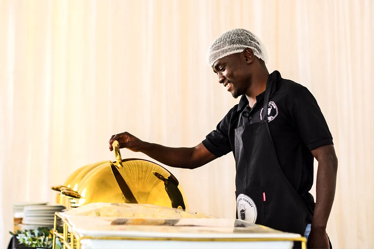 Caterer in a hairnet setting up a chafing dish for an event