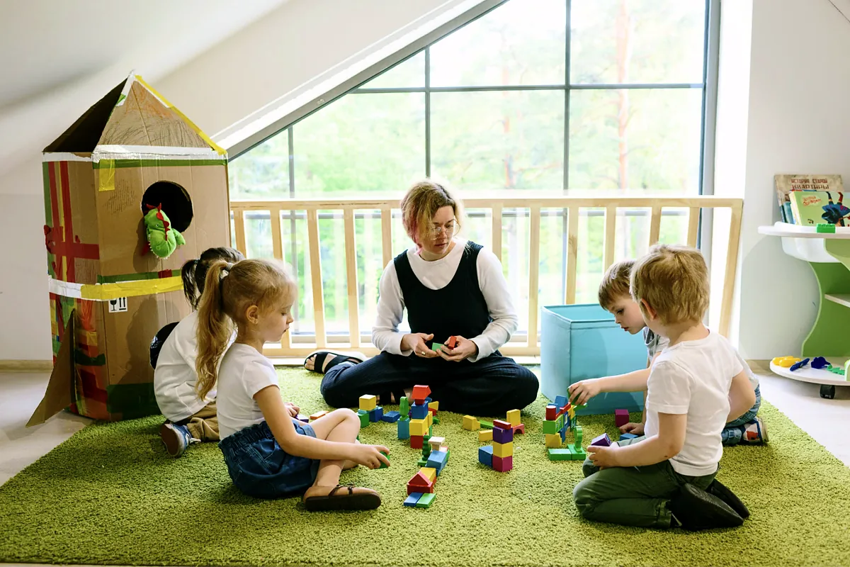 Teacher playing with young children on the floor of a bright classroom