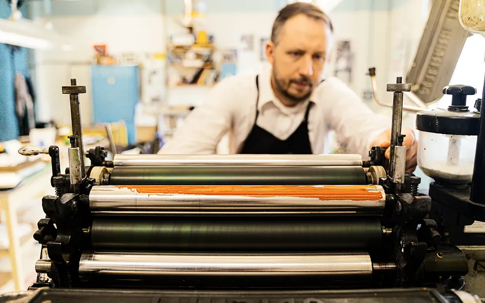 Press operator adjusting the inking rollers of a printing press