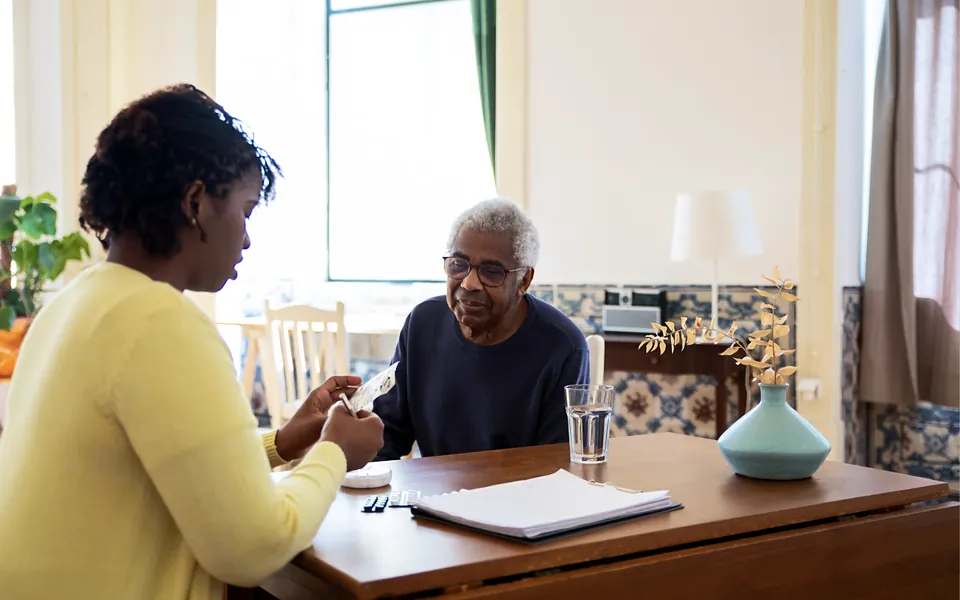Home care aide reviewing paperwork with an older man at his kitchen table
