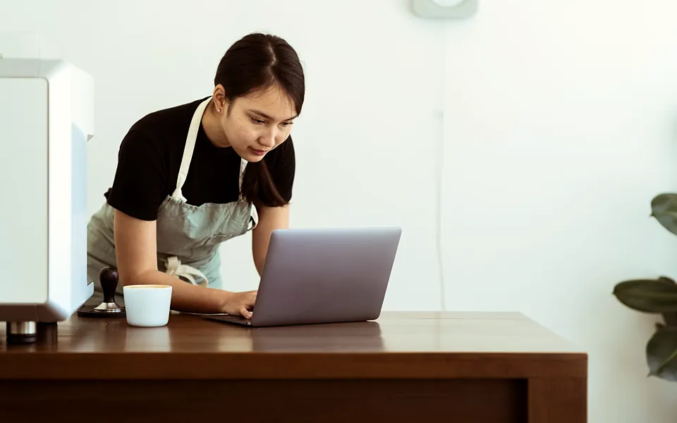 Café owner in an apron checking her laptop at the counter
