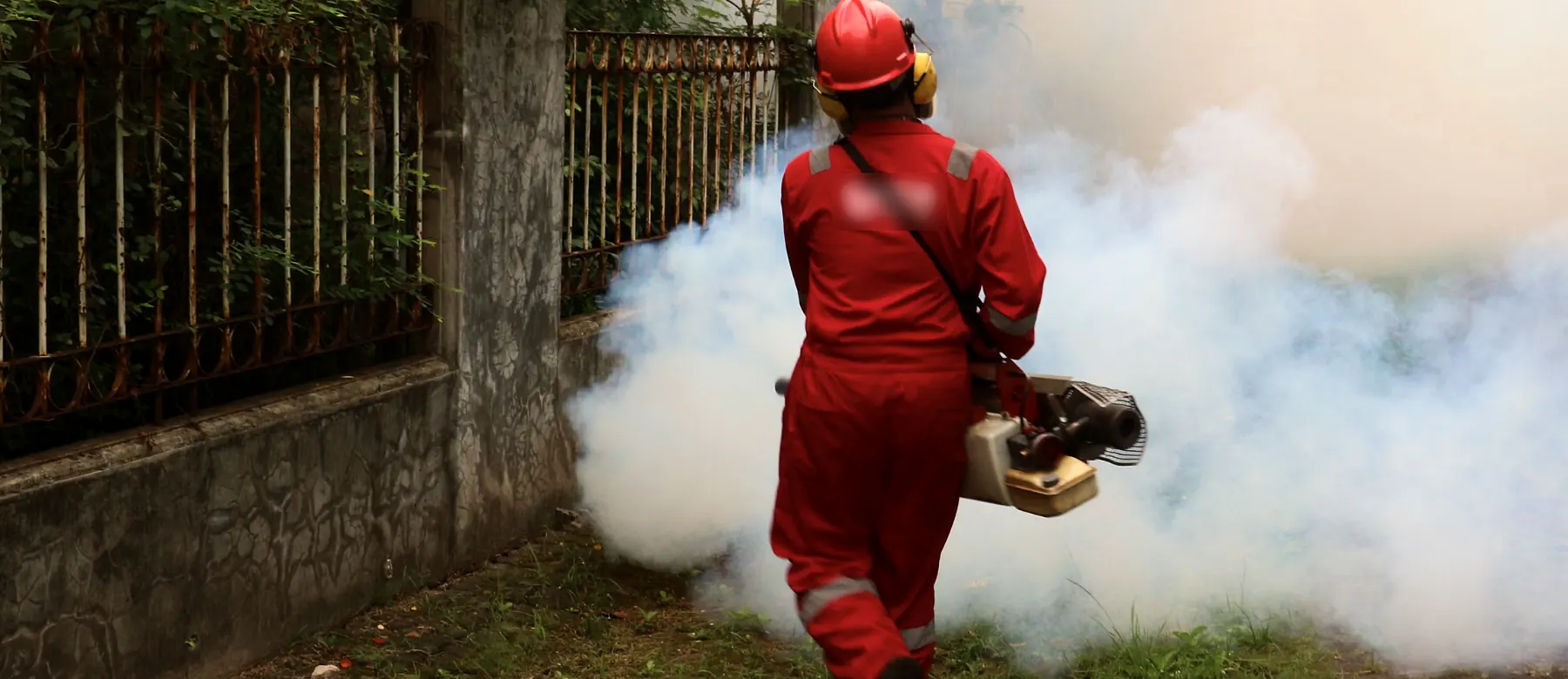 Pest control technician in protective gear fogging a yard