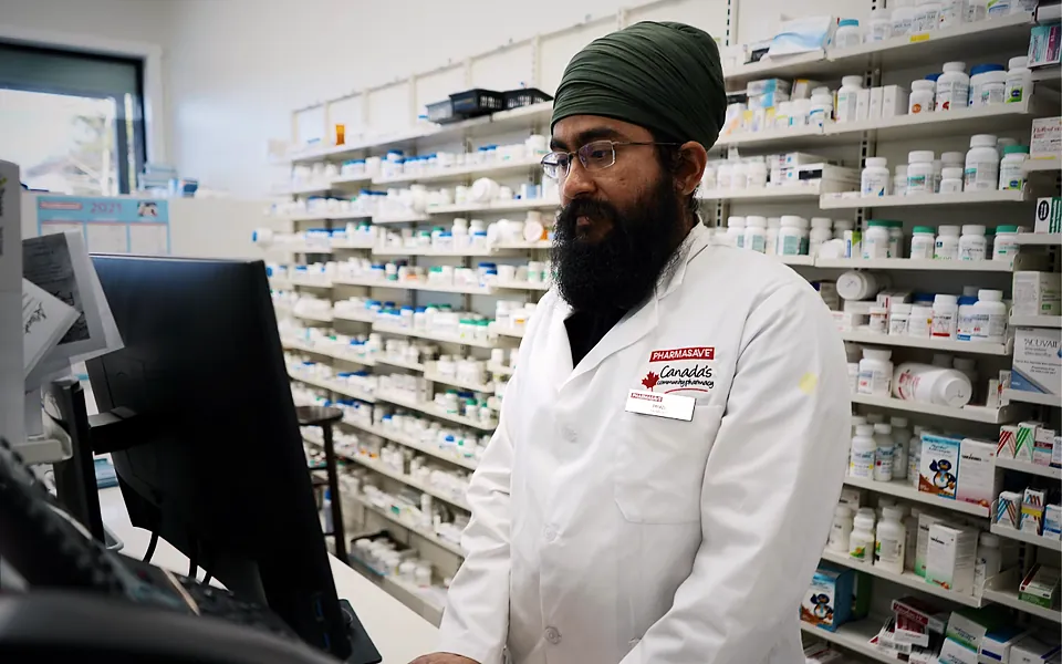 Pharmacist working at a computer in front of shelves of medication