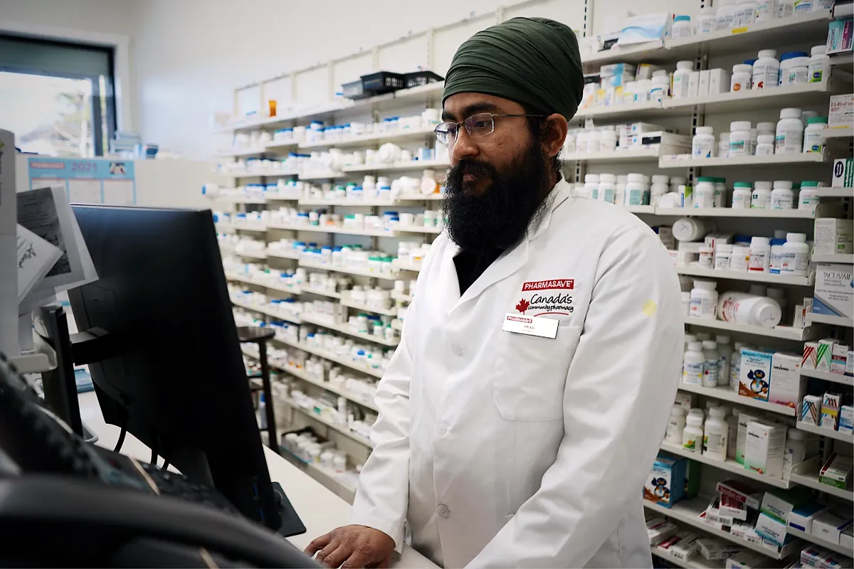 Pharmacist working at a computer in front of shelves of medication