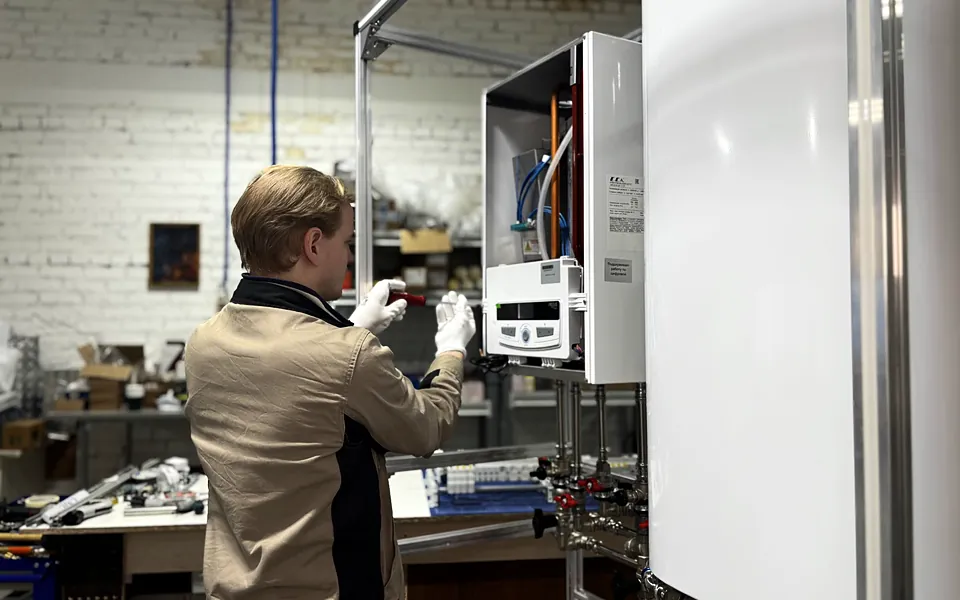 Technician installing a wall mounted boiler and water lines in a workshop