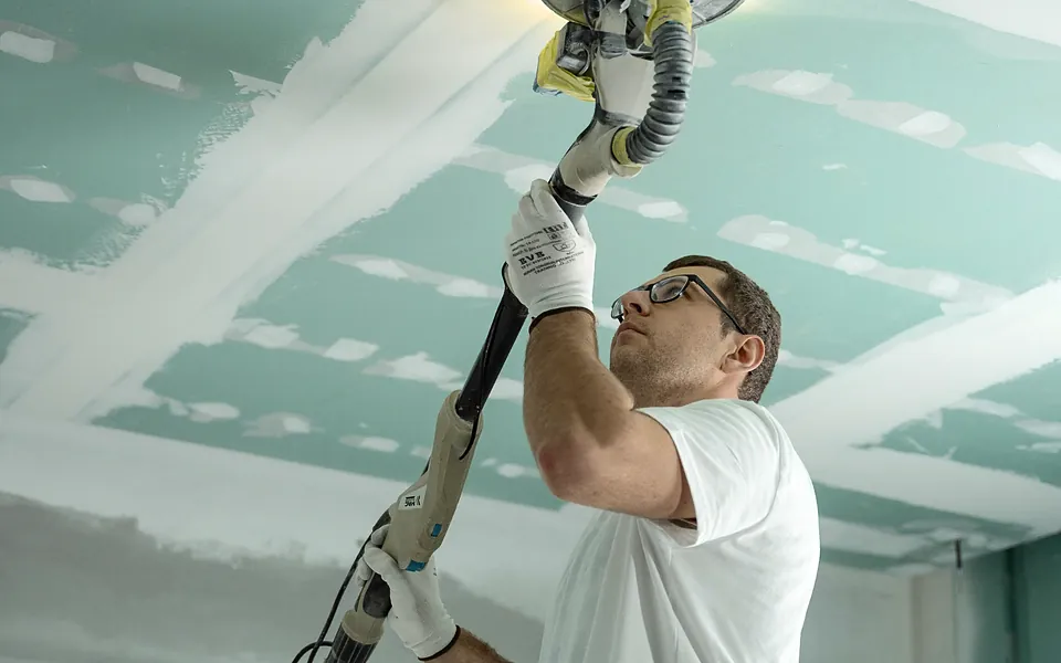 Contractor sanding a repaired drywall ceiling during a home rebuild