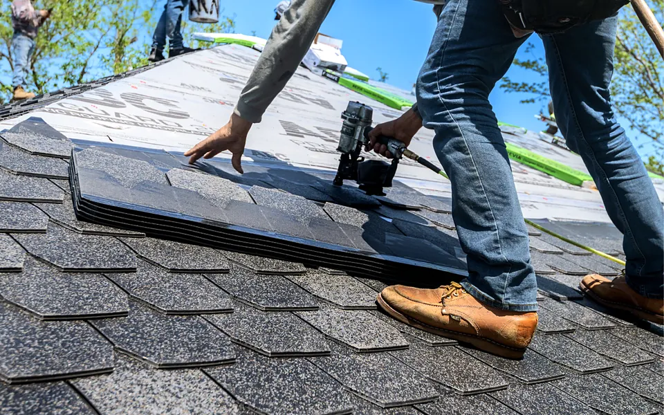 Roofer nailing asphalt shingles on a residential roof