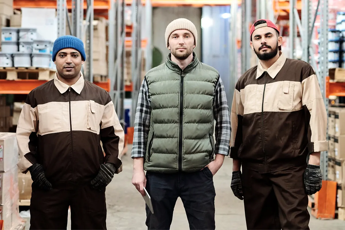 Three warehouse workers in work clothes standing in a stocked aisle