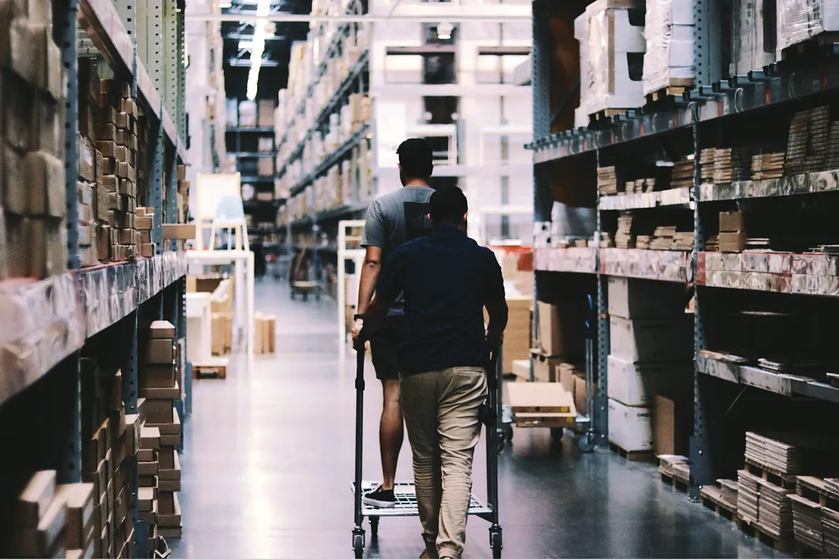 Two workers pushing a cart down a stocked warehouse aisle