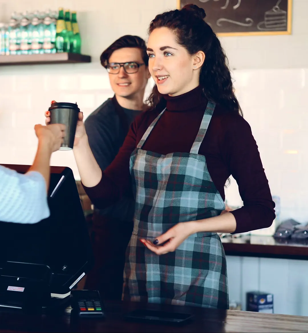 Café owner in a plaid apron serving a customer at the register