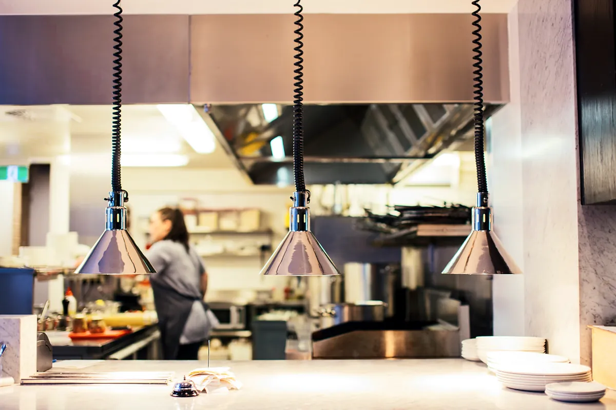 Commercial restaurant kitchen with a stainless steel hood and heat lamps over the pass