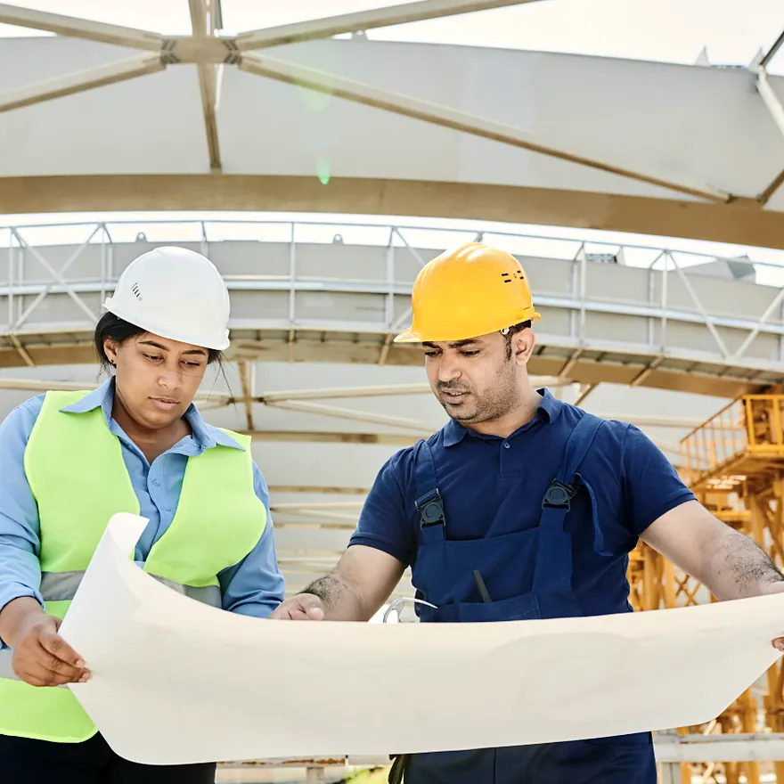 Two project leads in hard hats reviewing building plans at an expansion site