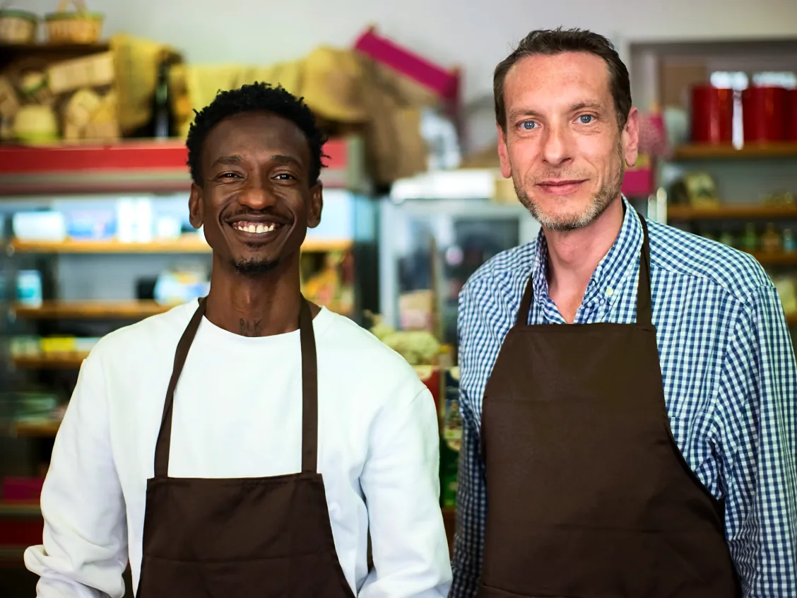 Two smiling retail store owners in aprons inside their shop